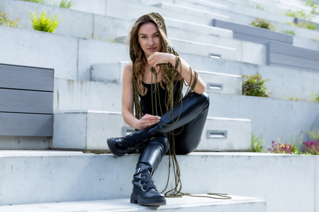 Sitting on modern concrete steps, she blends edgy fashion with fearless attitude. Leather, ropes and boots create a bold urban look â confident, untamed and unapologetically strongの写真素材