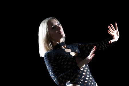 The Aesthetics of Dance in the Studio: Blonde Woman in a Black Bodysuit, Expressive Lines and Emotions Against a Black Backgroundの写真素材