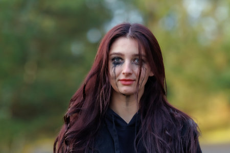 A close-up portrait of a young woman outdoors in autumn. Smeared makeup under her eyes creates a...
