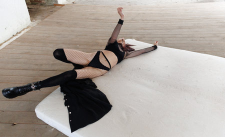 Alternative fashion scene with woman on worn mattress in empty abandoned room, showing expressive...