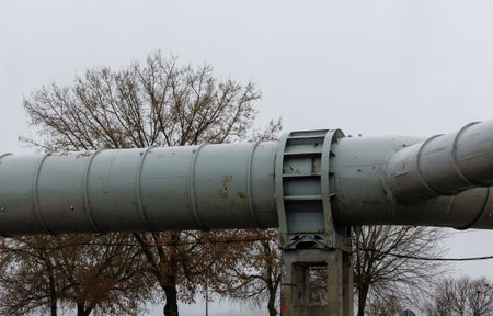 Large elevated industrial pipeline supported by concrete pillars on a cloudy day. Metal surface...