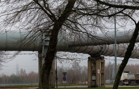 Large elevated industrial pipeline supported by concrete pillars on a cloudy day. Metal surface...