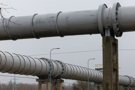 Large elevated industrial pipeline supported by concrete pillars on a cloudy day. Metal surface...