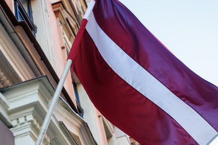 Latvian national flags displayed in the streets of Riga, Latvia, with modern and historic architecture visible in the background on a clear sunny day.の写真素材