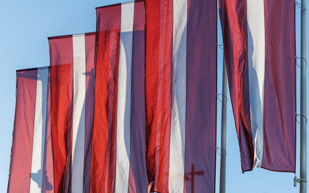 Latvian national flags displayed in the streets of Riga, Latvia, with modern and historic architecture visible in the background on a clear sunny day.の写真素材