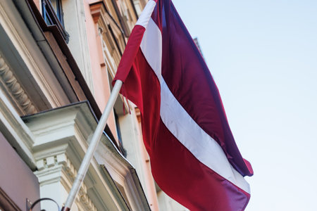 Latvian national flags displayed in the streets of Riga, Latvia, with modern and historic architecture visible in the background on a clear sunny day.の写真素材