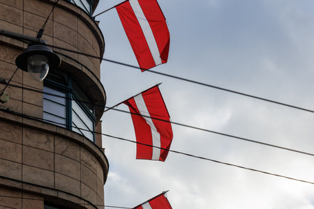 Latvian national flags displayed on building facades in an urban environment, waving in natural light. Red-white-red colors shown in various city streets and architectural settingsの写真素材