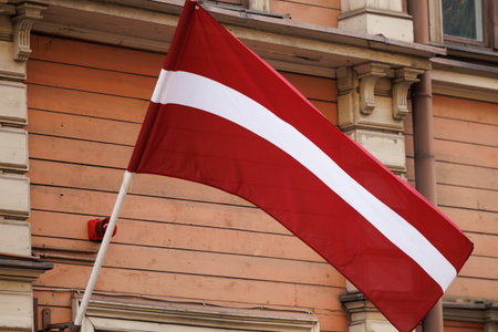 Latvian national flags displayed on building facades in an urban environment, waving in natural light. Red-white-red colors shown in various city streets and architectural settingsの写真素材
