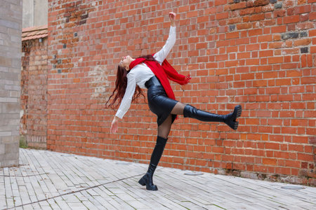 Dynamic portraits of a woman dancing in an urban alley with a brick wall background. Energetic movement, fashion details and expressive motion captured outdoors in natural lightの写真素材