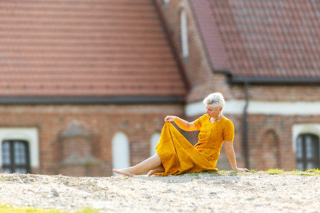 A woman in a yellow dress sits on the ground outdoors in a good moodの写真素材