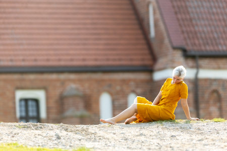 A woman in a yellow dress sits on the ground outdoors in a good moodの写真素材