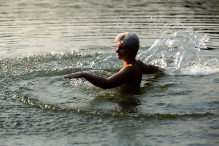 Happy woman in the sunset, splashing in the lake, warm autumn eveningの写真素材