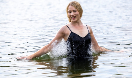 Expressive young woman performing graceful dance movements in calm water while wearing a flowing black dress. Concept of freedom, femininity, balance, emotional expression, body awareness and harmony with natureの写真素材