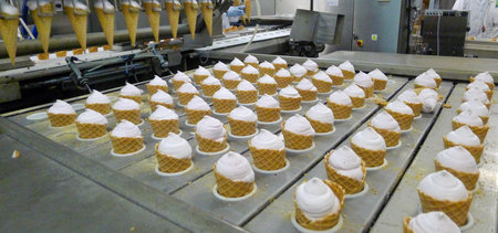 Industrial ice cream cone production line inside a food factory. Automated machinery fills waffle...