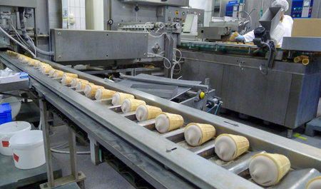 Industrial ice cream cone production line inside a food factory. Automated machinery fills waffle...