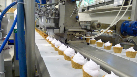 Industrial ice cream cone production line inside a food factory. Automated machinery fills waffle...