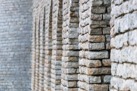 Historic stone wall with repeating vertical columns creating rhythm and depth. Natural masonry texture, perspective lines and neutral tones. Ideal architectural background, construction concept or minimalist design use.の写真素材