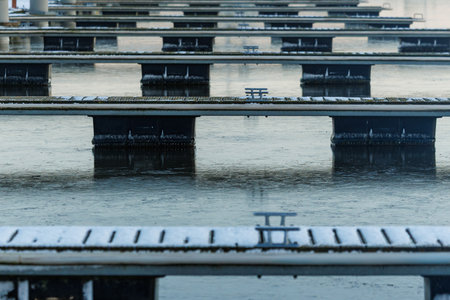 Empty marina in Nida harbor during winter. Floating piers covered with frost, calm water, cloudy sky and coastal landscape. No people, no boats. Cold season, silence, minimal maritime backgroundの写真素材