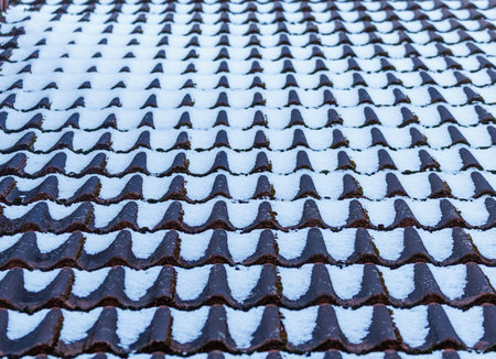 Snow covered tiled rooftops in winter. Traditional architecture with repeating roof patterns, cold weather and soft natural light. Clean winter scene suitable for seasonal and architectural conceptsの写真素材