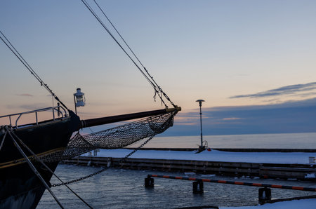 Close-up of fishing net and ship rigging against calm sea and winter harbor at dusk. Minimal...