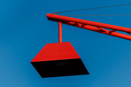 Minimalist close-up of a contemporary red street light structure with geometric lamp shade and cables, photographed against a clear blue sky in Tallinn, Estonia.の写真素材