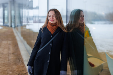 A business woman standing by a glass wall with her reflection on a cold winter day. Concept of...