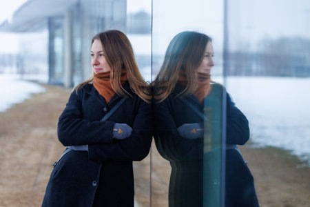 A business woman standing by a glass wall with her reflection on a cold winter day. Concept of...