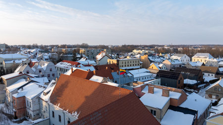 Lithuanian national flag waving above the snowy rooftops of Kedainiai old town during winter. Historic architecture, red tiled roofs and cold seasonal atmosphere in central Lithuania. Patriotic symbol, Baltic country, European cityscapeの写真素材