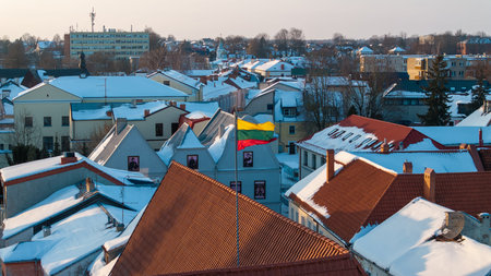 Lithuanian national flag waving above the snowy rooftops of Kedainiai old town during winter. Historic architecture, red tiled roofs and cold seasonal atmosphere in central Lithuania. Patriotic symbol, Baltic country, European cityscapeの写真素材