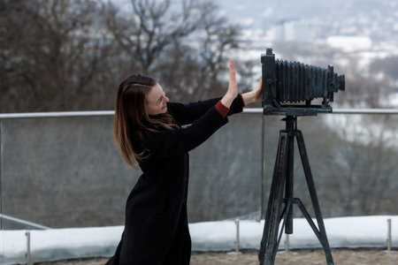 Smiling young woman interacting with vintage large format camera outdoors in winter. Concept of...