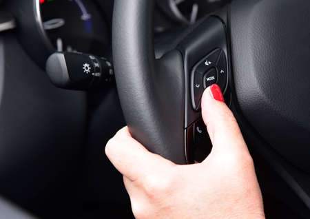 Female finger on volume control button on car steering wheel