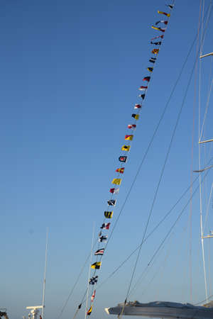 Flags of different countries hanging on the mast of a sailboat in Ibiza