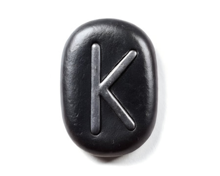A single, dark, oval-shaped stone featuring a carved letter K. Isolated on a white background.の素材