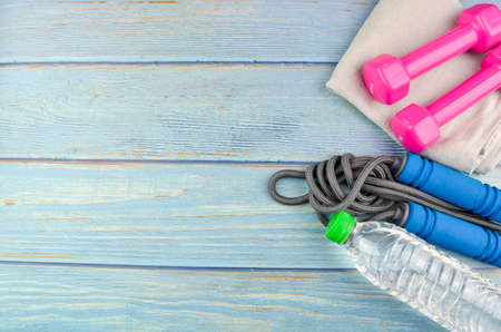 Top or flat lay view of dumbbells, towel, water and skipping rope with copy space area on blue...