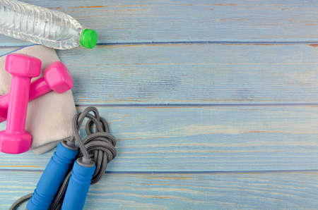 Top or flat lay view of dumbbells, towel, water and skipping rope with copy space area on blue...