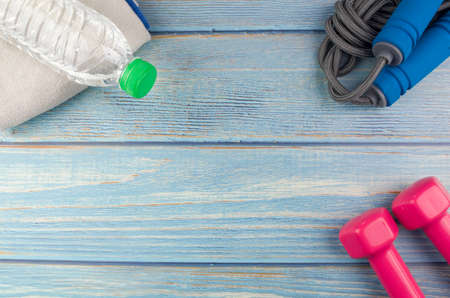 Top or flat lay view of dumbbells, towel, water and skipping rope with copy space area on blue wooden background. Healthy concept. Selective focus.の写真素材