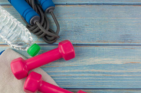 Top or flat lay view of dumbbells, towel, water and skipping rope with copy space area on blue...