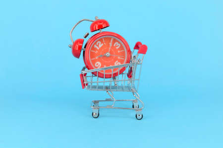Shopping cart and classic alarm clock on blue background. Sale time market shop consumer concept....