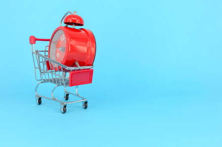 Shopping cart and classic alarm clock on blue background. Sale time market shop consumer concept....