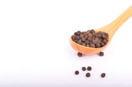 Black peppers on wooden spoon isolated on white background. Selective focus.