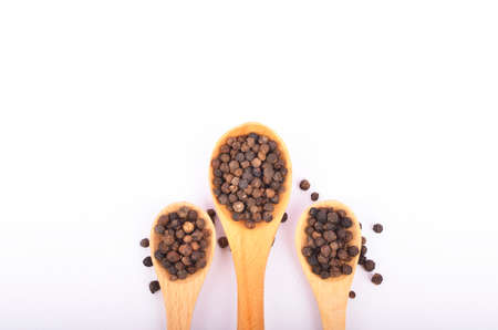Black peppers on wooden spoon isolated on white background. Selective focus.