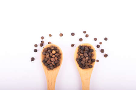 Black peppers on wooden spoon isolated on white background. Selective focus.