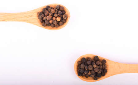 Black peppers on wooden spoon isolated on white background. Selective focus.
