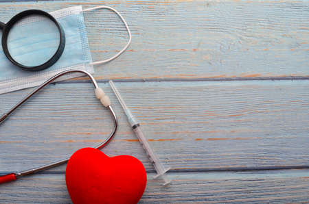 Red heart, face mask, stethoscope and syringe on wooden background. Health concept.の写真素材