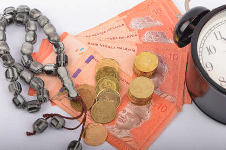 Rosary, coins in a gunny sack and alarm clock. Islamic banking/finance concept on over white background. Selective focus.の写真素材