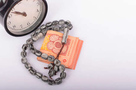 Rosary, coins in a gunny sack and alarm clock. Islamic banking/finance concept on over white background. Selective focus.の写真素材