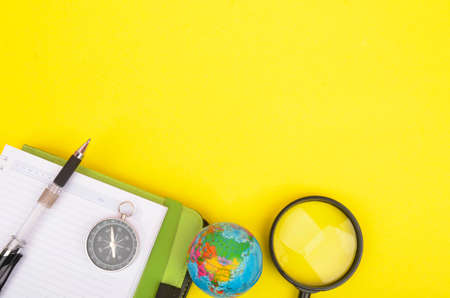 conceptual image. Notebook, compass, magnifying glass, pen and world globe on yellow background.