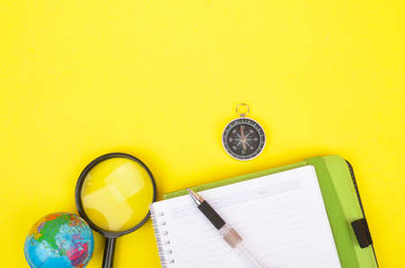 conceptual image. Notebook, compass, magnifying glass, pen and world globe on yellow background.の写真素材