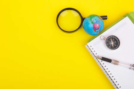 conceptual image. Notebook, compass, magnifying glass, pen and world globe on yellow background.の写真素材