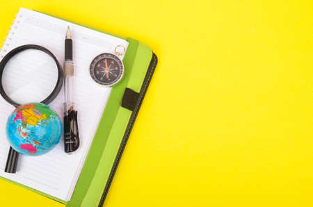 conceptual image. Notebook, compass, magnifying glass, pen and world globe on yellow background.の写真素材